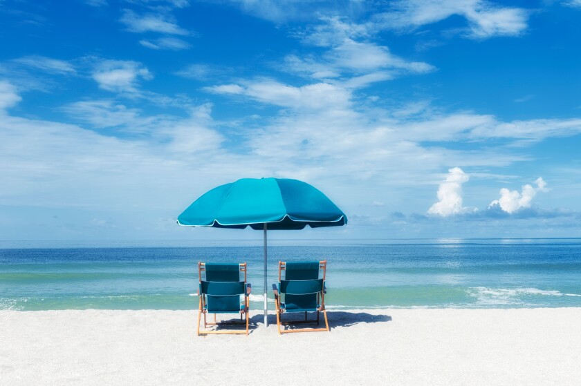 Two turquoise beach chairs under umbrella facing the ocean sea shore under sunny warm blue sky blue-green ocean