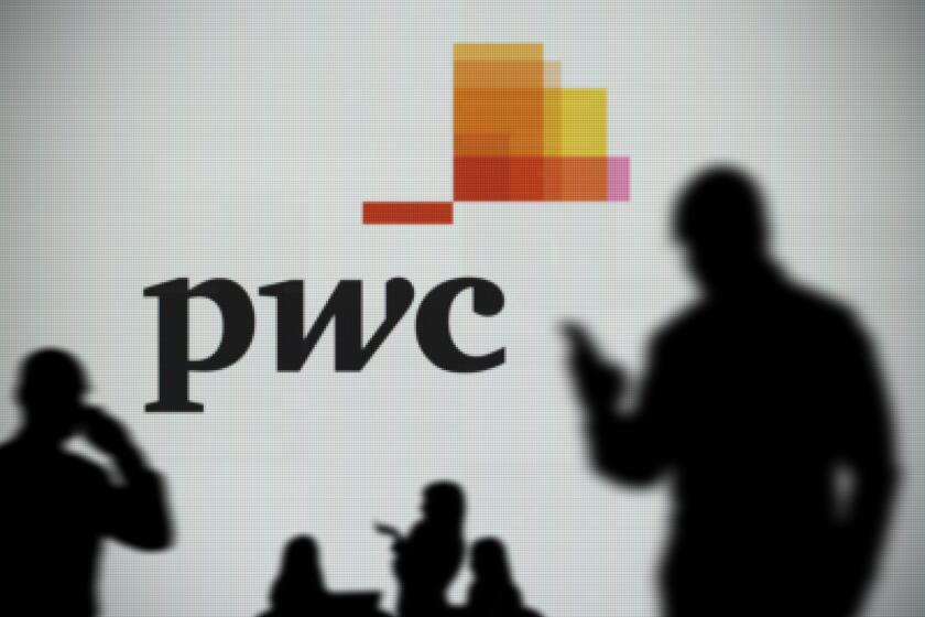 The PWC logo is seen on an LED screen in the background while a silhouetted person uses a smartphone in the foreground (Editorial use only)