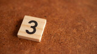 Wooden tile with the prime number 3 on a rustic brown surface, mathematical concept with copy space for education and numeracy