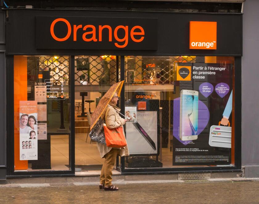 A woman with an orange umbrella and bag outside the Orange phone store in Dieppe, Normandy, France, Europe
