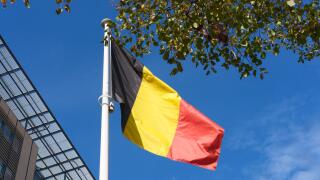 Belgian flag swaying in the wind against blue sky and trees. Flag of Belgium near train station. Flag day celebration. Embassies and consulates