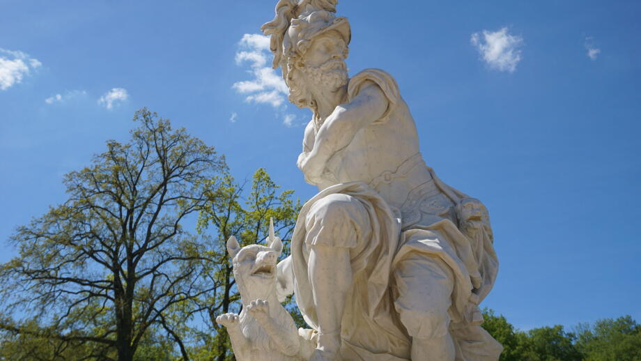 A marble statue of Mars or Ares, the ancient Roman/Greek god of war, with a dog stands in the castle garden park of Sanssouci Palace, Potsdam, Germany