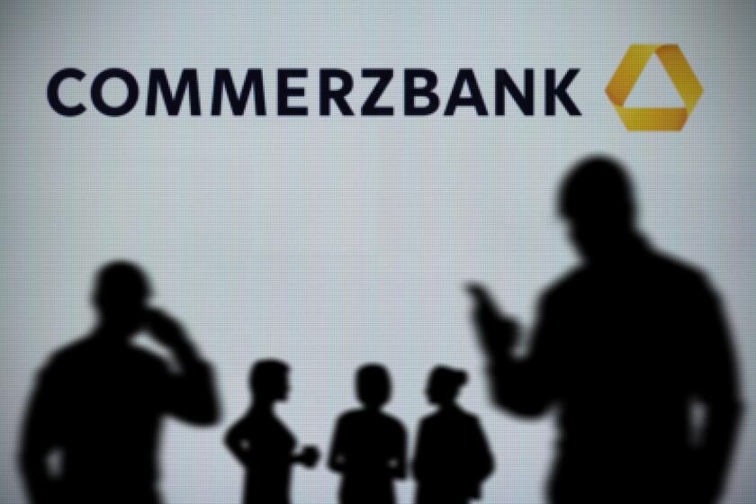 The Commerzbank logo is seen on an LED screen in the background while a silhouetted person uses a smartphone in the foreground (Editorial use only)