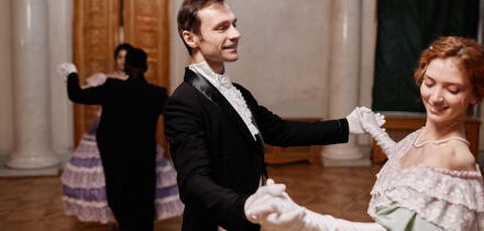 Portrait of smiling gentleman wearing classic tailcoat dancing with young lady during debutante ball in palace, copy space
