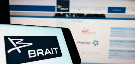 Cellphone with logo of investment company Brait SE on screen in front of business website. Focus on center-right of phone display.