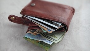 we see a brown leather wallet over packed with different currency and credit cards on a pale marble surface