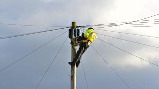 A British Telecoms engineer installing fibre optic cable at the top of a telephone pole England UK