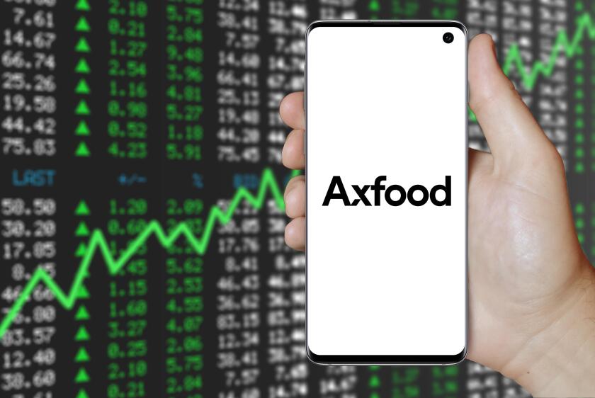 A man holds a smartphone displaying the logo of company Axfood listed on OMX Stockholm. Positive stock market background. Credit: PIXDUCE