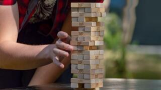 Guy sticks out wooden block from  tower of game jenga. Side front view. Concept. Surgut, Russia - September 25, 2019.