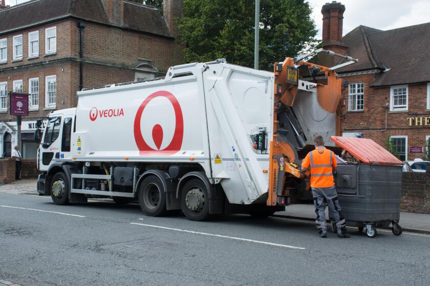 Veolia dustbin lorry (dustcart) with worker emptying a large waste bin on the street. binman, binmen