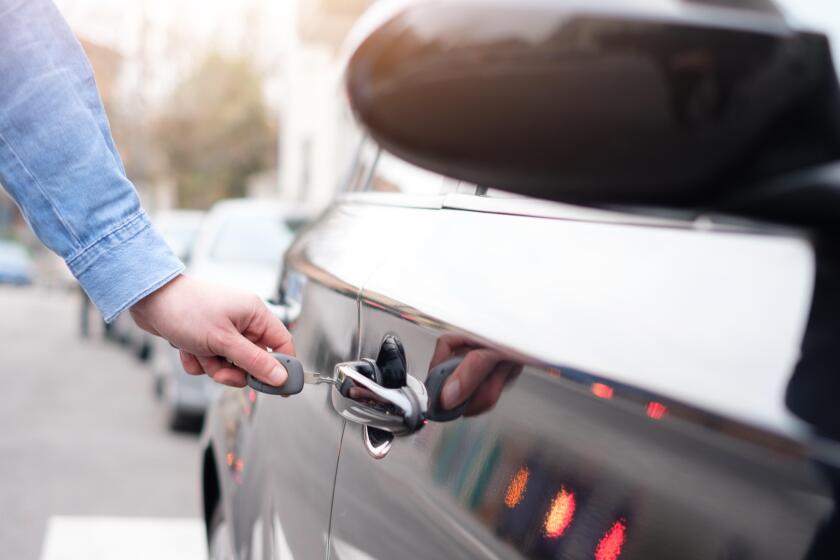 Hand holding a car key and opening the car door lock