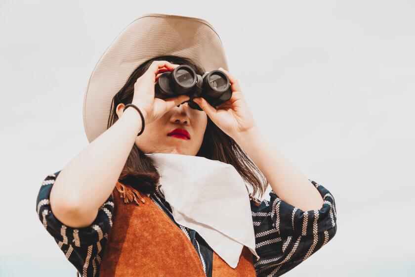 cute chinese cowgirl while looking at the horizon with binoculars on a wild west farm