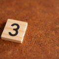 Wooden tile with the prime number 3 on a rustic brown surface, mathematical concept with copy space for education and numeracy
