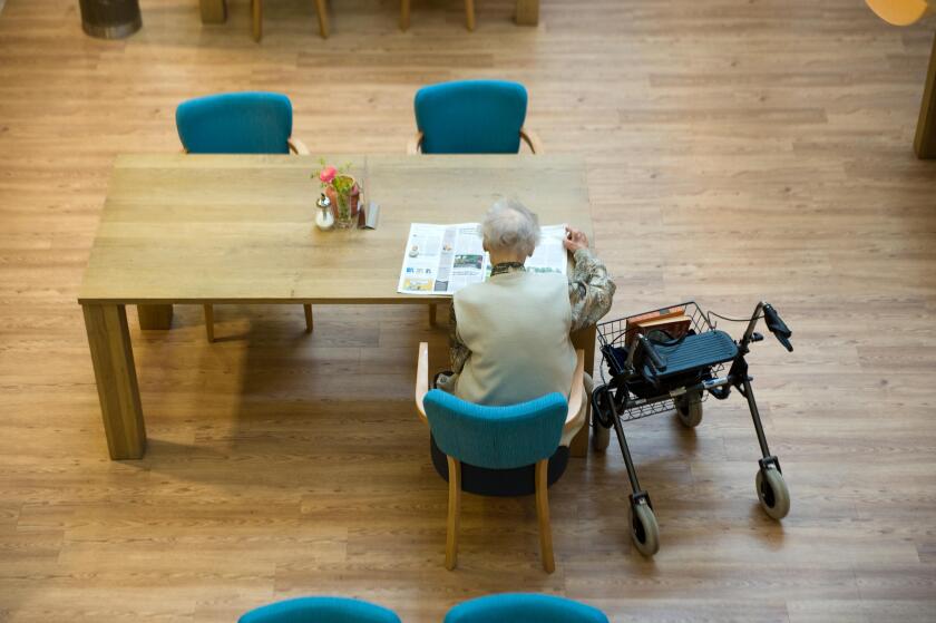 ALMELO, THE NETHERLANDS - JUNE 14, 2016: An elderly woman is reading a newspaper on the table of an elderly home.
