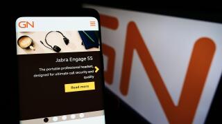 Person holding smartphone with website of Danish electronics company GN Store Nord AS on screen with logo. Focus on center of phone display.