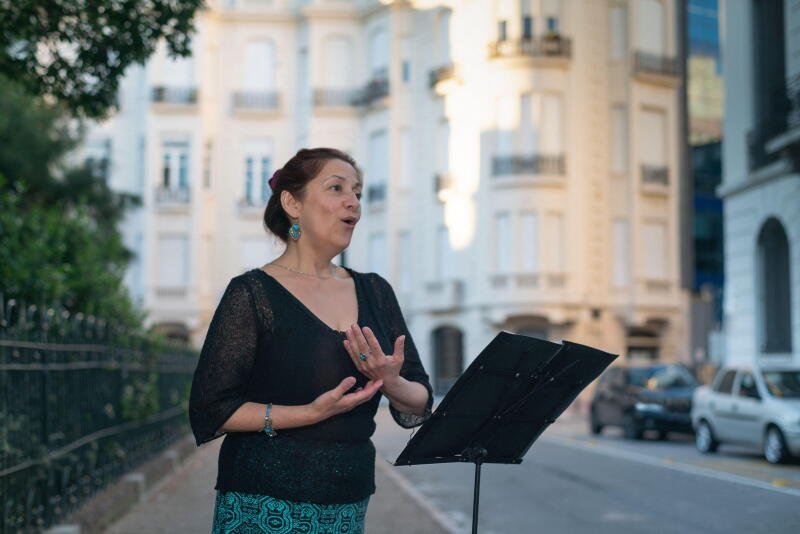 Soprano sings opera on an elegant street with a music stand