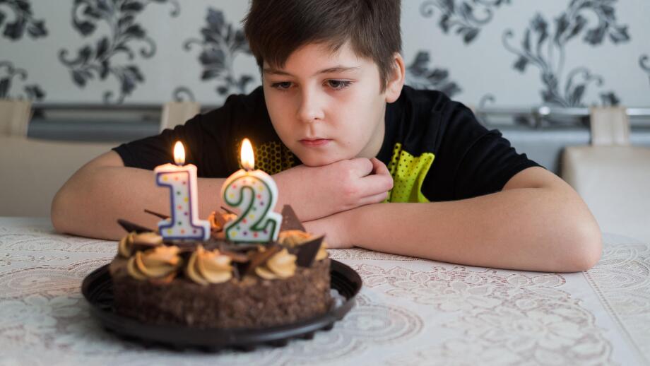 Teen boy looks thoughtfully at cake with candles on twelfth day of birth