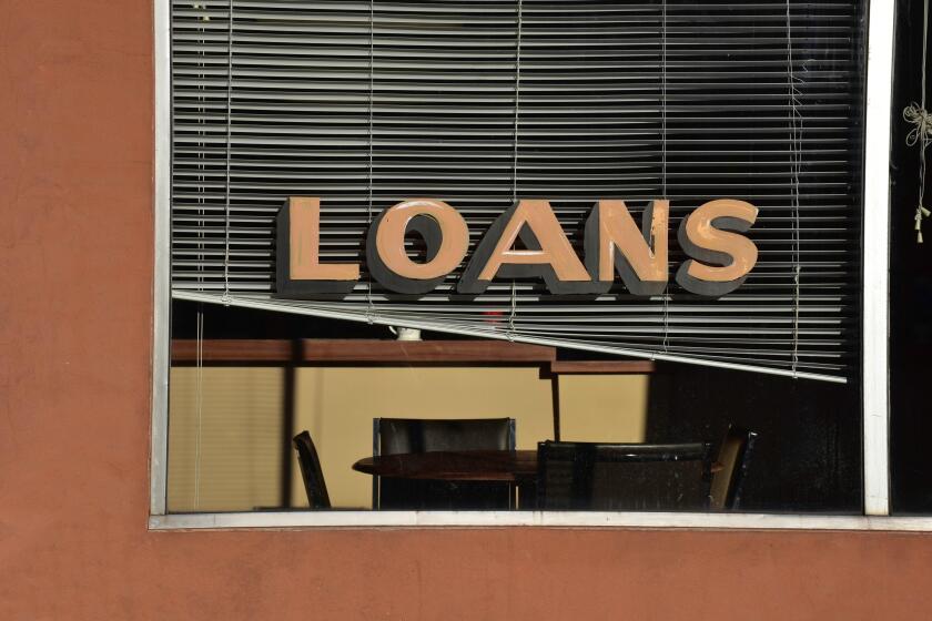 A quiet scene in a small town shows a loans sign in the window of a financial services storefront.