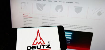 Person holding cellphone with logo of German engine company Deutz AG on screen in front of business webpage. Focus on phone display.
