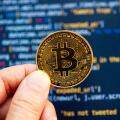 Hand holding a Bitcoin coin in front of computer code representing cryptocurrency development