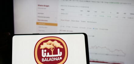 Person holding mobile phone with logo of Qatari dairy and food company Baladna in front of business web page. Focus on phone display.