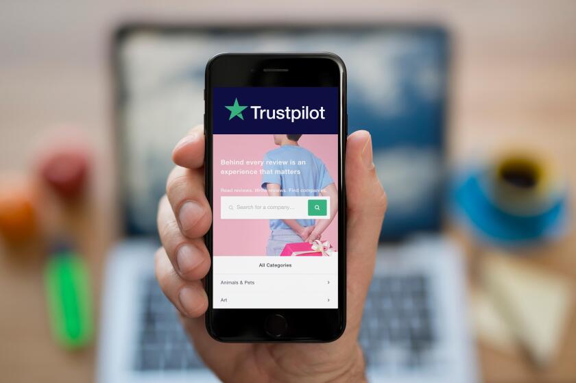 A man looks at his iPhone which displays the Trustpilot logo (Editorial use only).