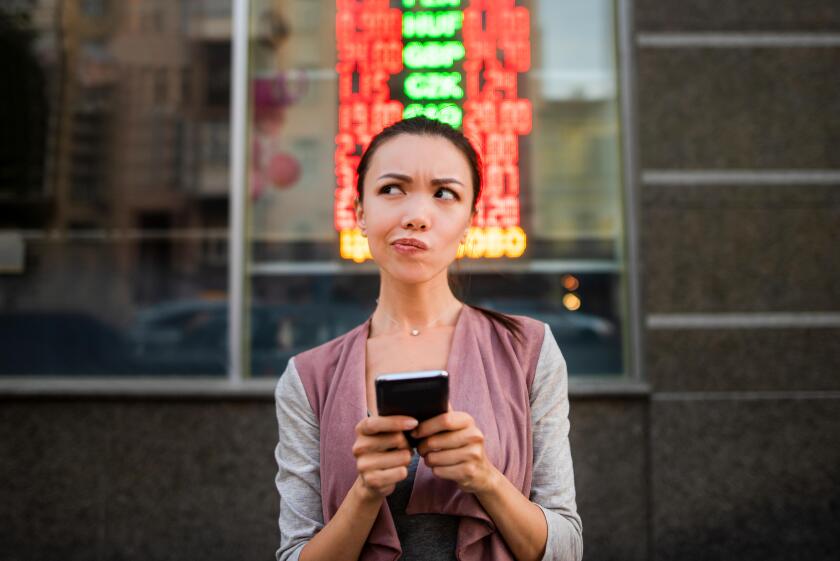 A young beautiful asian woman using an application in her smart phone to check currency exchange rates in front of an illuminated information board.