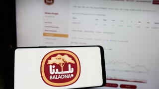 Person holding mobile phone with logo of Qatari dairy and food company Baladna in front of business web page. Focus on phone display.