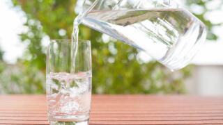 Drinking water flowing from a glass jug into a glass ? background with plants