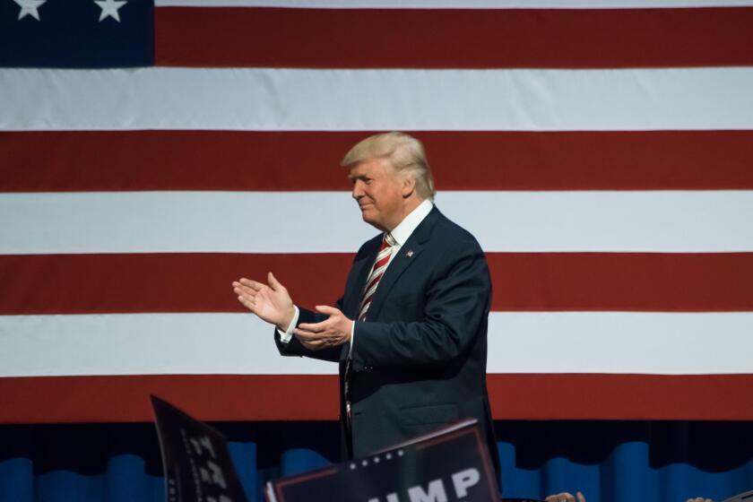 Republican Presidential Nominee Donald Trump walking on stage applauding the crowd near the American Flag.