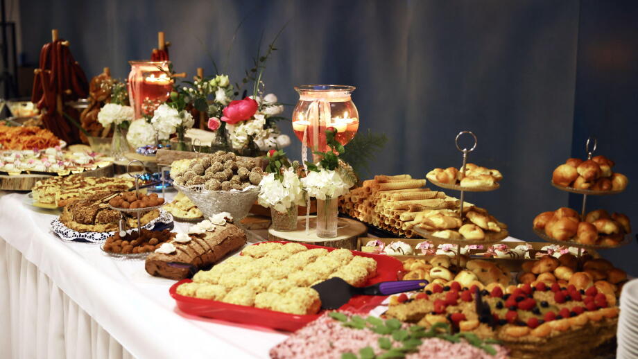 Lavishly decorated dessert buffet table with a variety of pastries, cookies, cakes, and sweets, beautifully arranged with floral decor.