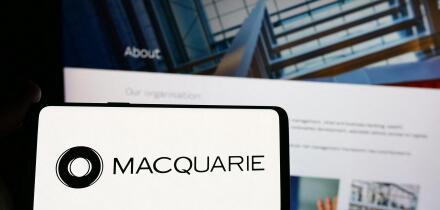 Person holding smartphone with logo of Australian financial company Macquarie Group Limited in front of website. Focus on phone display.