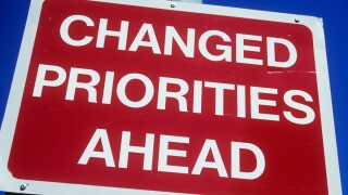 Close up of red and white road sign on a lamp post or pole against clear blue sky stating Changed priorities ahead. Image shot 2006. Exact date unknown.