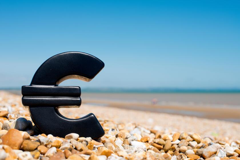The Euro symbol sitting on a pebble beach against a clear blue sky.