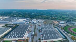 Drone shot of two large warehouse buildings near national highway across newly developed commercial real estate properties surrounded by lush greenery