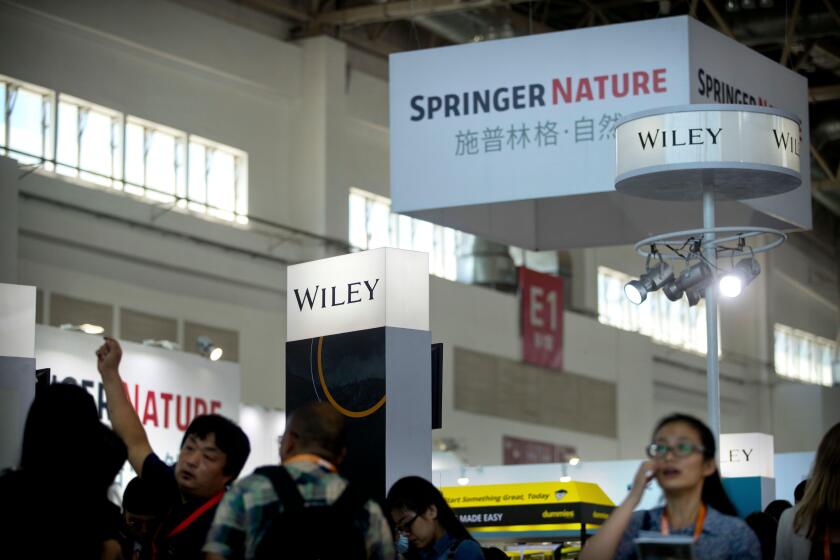 In this Aug. 23, 2017, photo, visitors browse vendor exhibits near a display from publisher Springer Nature at the Beijing International Book Fair in Beijing. Academic publisher Springer Nature said Wednesday, Nov. 1, 2017, that it has blocked access to a