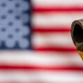 A close up of a piece of metal pipe from which oil is pouring, against the backdrop of an American flag. Mineral oil on factory on background of unite