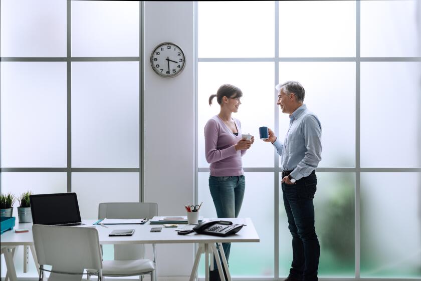 Cheerful office workers in the office, relaxing, having a coffee break and chatting together, they are standing in front of the