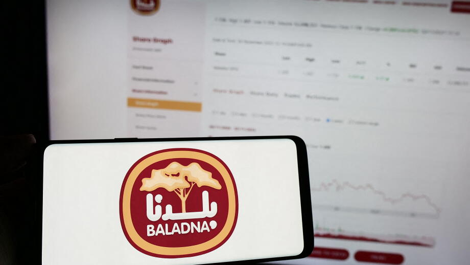 Person holding mobile phone with logo of Qatari dairy and food company Baladna in front of business web page. Focus on phone display.