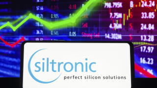 In this photo illustration the Siltronic AG logo seen displayed on a smartphone screen, with graphic representation of the stock market in the backgro