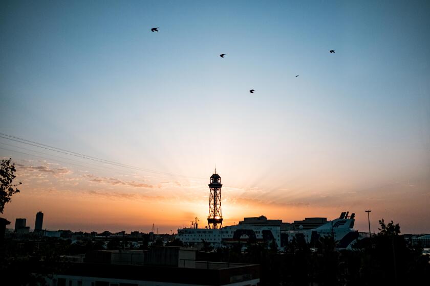 montjuic cableway tower at dawn with sun rising behind tower during sunrise with spectacular rays, a landmark of barcelona with the port and cruise sh