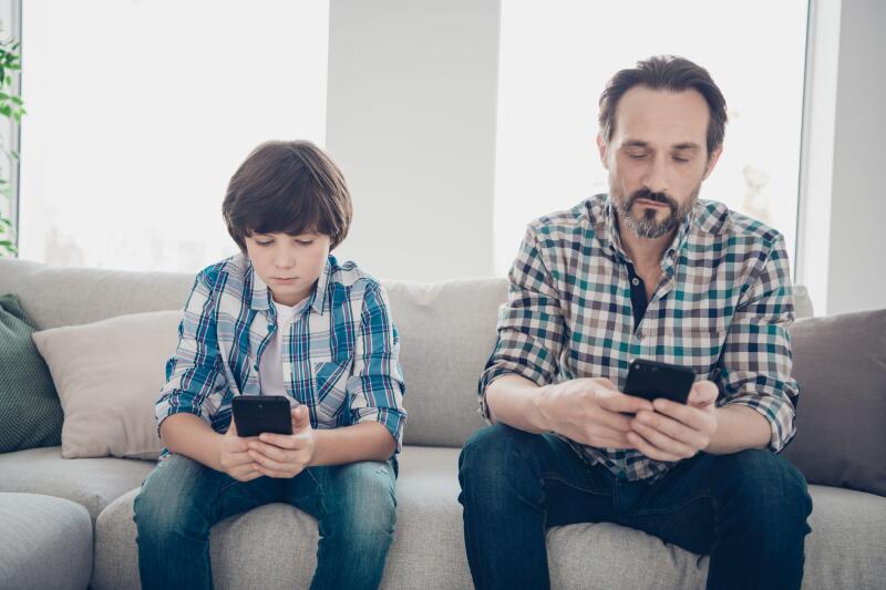 Do not leave in virtual life spend time with your relatives concept. Photo of serious kid and his bearded in checkered shirt dad holding telephones in