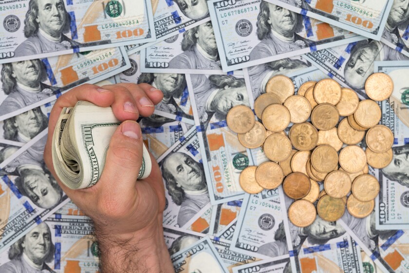 Conceptual financial image of a man clutching a wad of dollar bills over a background of multiple scattered new 100 dollar bills