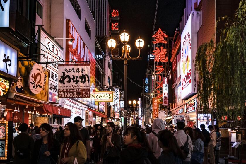 Crowd of tourists strolling down one of the streets in Osaka's Dotonbori area. Cityscape by night with lots of billboards and lights.