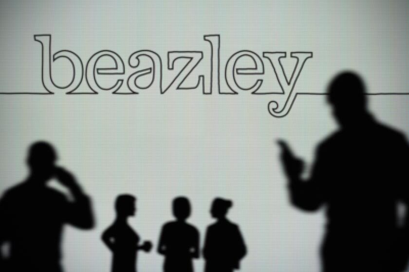 The Beazley Group logo is seen on an LED screen in the background while a silhouetted person uses a smartphone (Editorial use only)