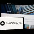 Person holding smartphone with logo of Australian financial company Macquarie Group Limited in front of website. Focus on phone display.
