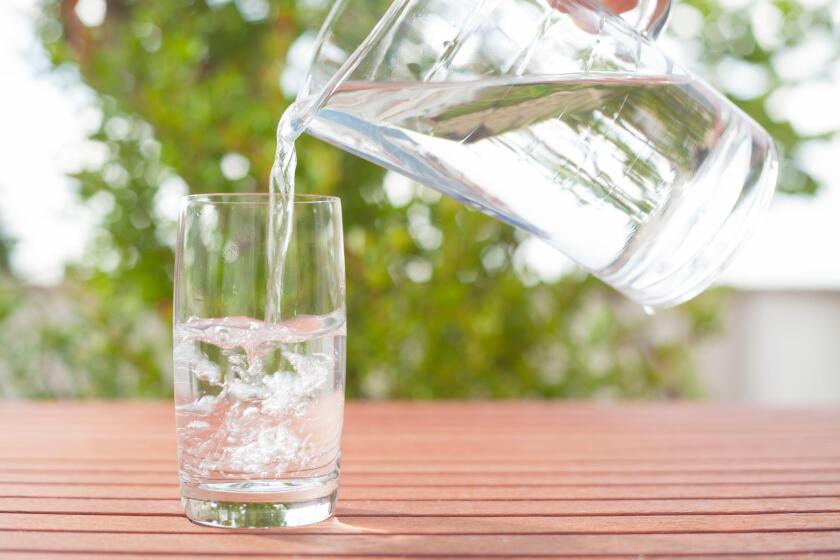 Drinking water flowing from a glass jug into a glass ? background with plants