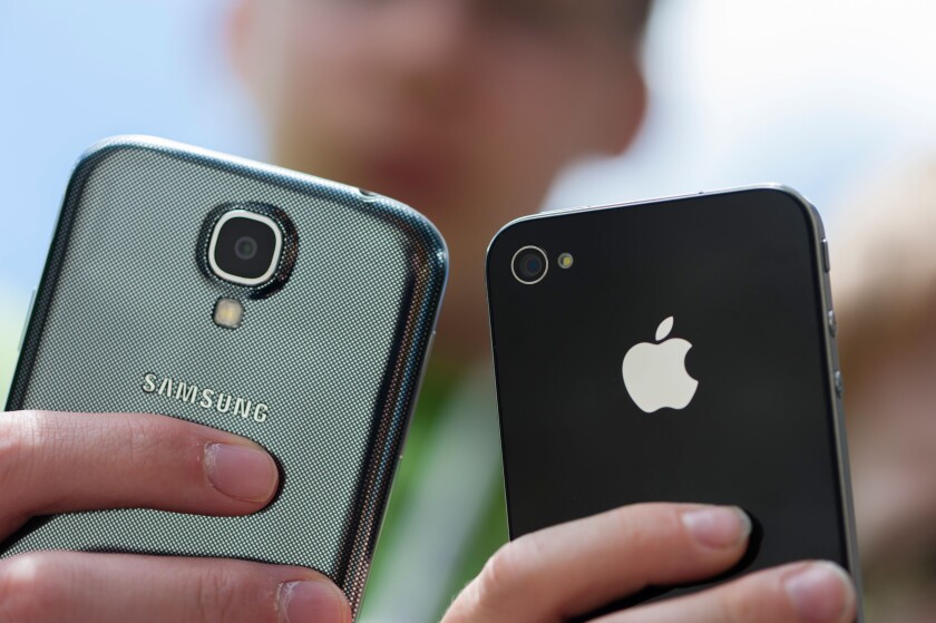 Two teenagers are posing with their Samsung Galaxy S4 (left) and iPhone 4 smartphones.