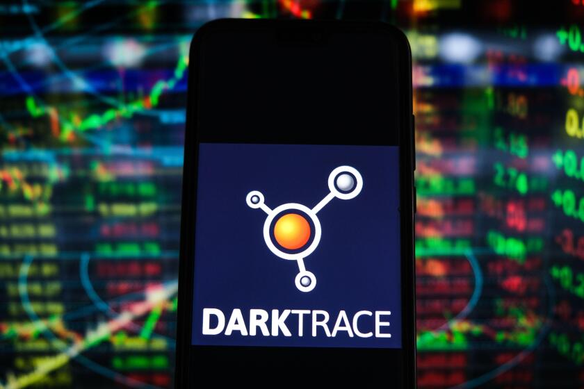 In this photo illustration a Darktrace logo seen displayed on a smartphone with stock market percentages in the background.