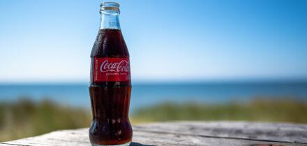 A coca-cola bottle against a sea and blue sky background in summer